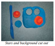 Clay cutting tool next to a rectangle of clay with two holes and one cone, the holes matching cones that have been cut out and placed on one side.