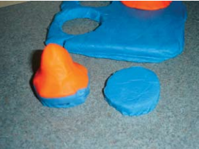 Close up of project. Rectangle of blue clay with orange cones on top, one of the cones has been cut out, as has an equal sized section of the background piece.